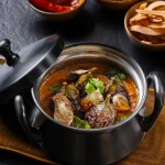 Brinjal curry in metal pot with curry leaves and red chillies